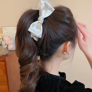 Detailed view of large white satin polka dot bow hair clip styled in a ponytail