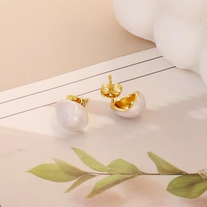 Macro shot of gold teardrop earrings with white enamel finish and butterfly backs