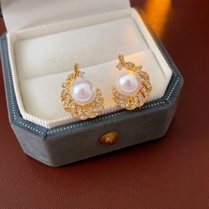 Macro shot of gold feather earrings with cubic zirconia and white pearl in a luxury box