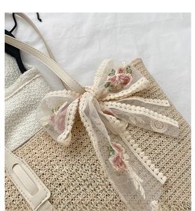 Detail of hand-woven straw tote bag with floral embroidery and lace bow decoration