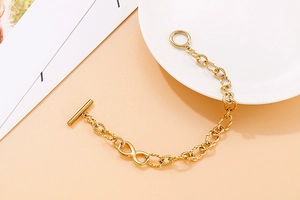 Detail of gold infinity charm bracelet with a toggle OT clasp on a white plate