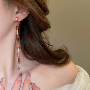 Detail of long drop earrings with pink strawberry quartz beads and golden tassels