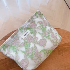 Close-up of floral embroidery and brand label on a white mesh makeup pouch