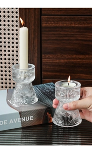 Detail of vintage ribbed glass candle holder with warm lit candle on decorative books