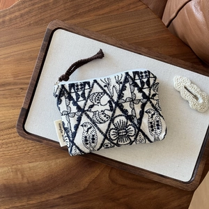 Macro detail of bird embroidery on beige linen coin purse with a woven zipper pull