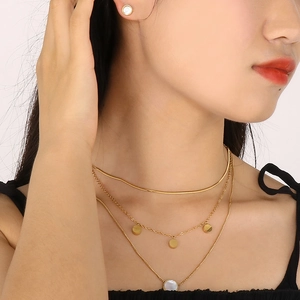 Close-up of model wearing triple-layered gold necklaces and white shell stud earrings