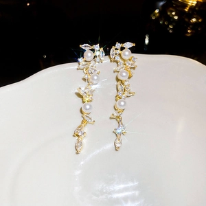 Macro view of gold tassel earrings with pearls and crystal leaf detail on a white plate