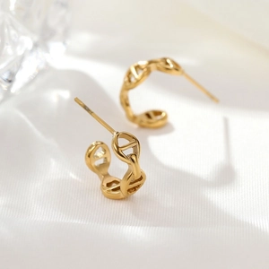 Matte goldene hohle geometrische Ankerkette-Ohrstecker auf weißem Seidenhintergrund