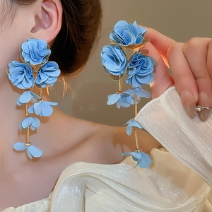 Close-up of blue fabric flower earrings with long gold tassels on model's ear