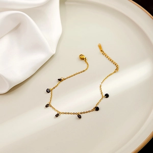 Detailed view of a gold chain bracelet with black circular charms on ceramic tray