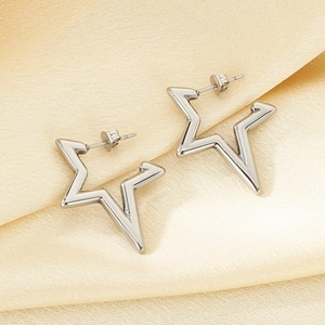 Dettaglio degli orecchini a stella in argento lucido su un elegante tessuto di seta beige