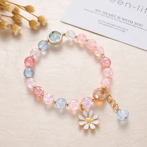 Close-up of pink and blue beaded crystal bracelet with white daisy pendant on beige texture