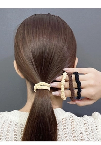 Close-up of four pleated fabric scrunchies in beige, brown, and black colors on a ponytail