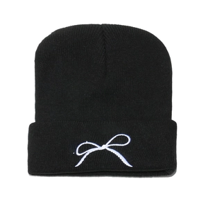 Close-up of black knitted beanie featuring white bow embroidery and thick texture