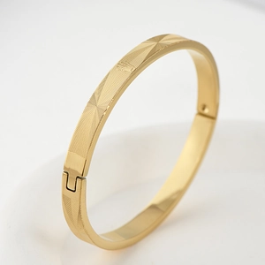 Detail of gold titanium steel bangle showing geometric diamond texture and hinge clasp