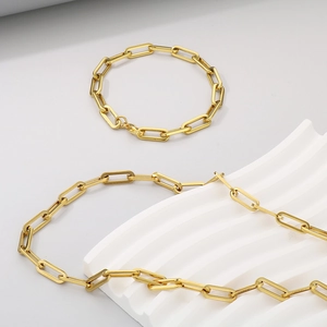 Detailed view of golden paperclip chain necklace and bracelet on a wavy display stand