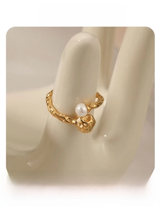 Gros plan d'une bague dorée texture lave avec une perle blanche sur un modèle de main