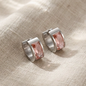 Macro view of silver huggie earrings with rectangular pink gemstones on linen