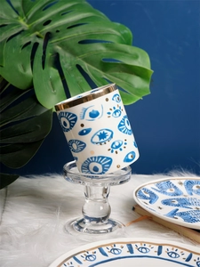 Detail of white ceramic eye mug with gold rim displayed on a glass candle holder
