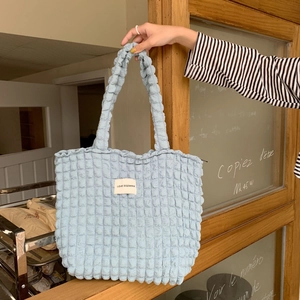 Dettaglio del tessuto a bolle azzurro e dell'etichetta con logo sulla borsa a spalla in tela
