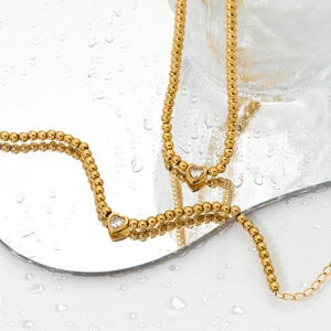 Collier à billes dorées avec pendentif cœur sur miroir réfléchissant et gouttes d'eau
