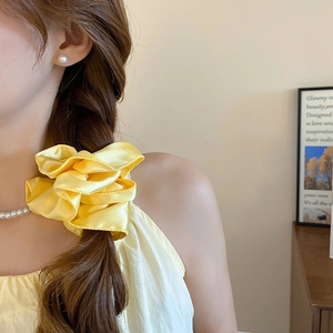 Detail view of a pale yellow satin bow hair tie worn on a stylish braided hairstyle