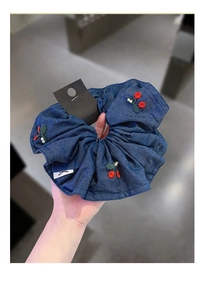 Detailed close-up of dark blue denim scrunchie with embroidered cherry and pearl accents