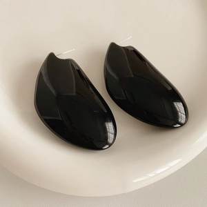 Vue macro de boucles d'oreilles noires en résine aux formes géométriques lisses sur céramique