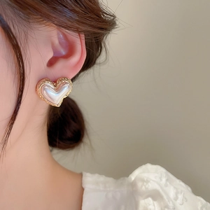 Close-up of heart-shaped pearl earrings with gold irregular edges on a female model