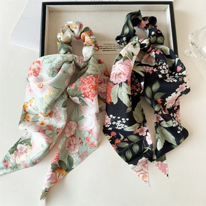 Detailed view of mint green and black floral satin scrunchies with long ribbons on a tray