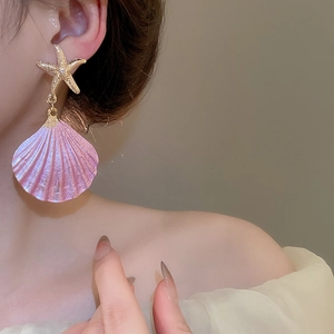 Close-up of pink shell and gold starfish earrings worn by a model in soft lighting