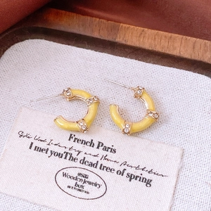 Macro detail of yellow enamel C-shaped earrings with gold frame and sparkling diamonds
