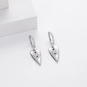Close-up of heart-shaped silver earrings with opal center and radial eye texture details