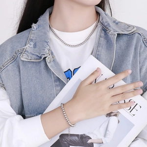 Détail d'un ensemble collier et bracelet à billes argentées porté avec une veste denim