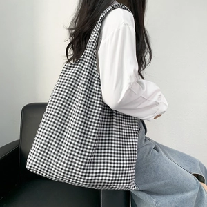 Side view of a large black and white checkered canvas tote bag worn by a model