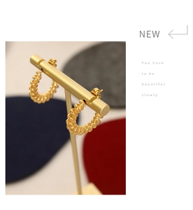 Detail view of gold-plated twisted C-shape hoop earrings on a T-bar display stand