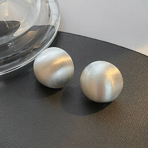 Macro detail of matte silver sphere earrings with brushed metal texture on black leather