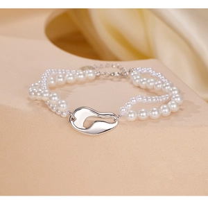 Dettaglio di bracciale a due fili di perle con inserto argentato su sfondo di seta beige