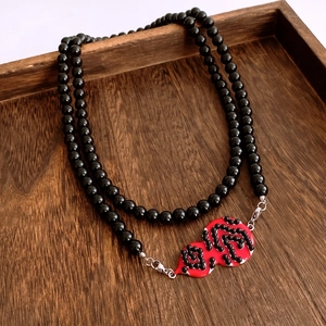 Detail of beaded necklace with red gourd pendant on a dark wooden tray display