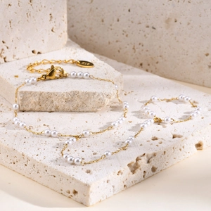 Detail view of gold layered snake chain with small white pearls on stone background
