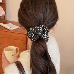 Detail of a black and white leopard print fabric scrunchie styled on a low ponytail