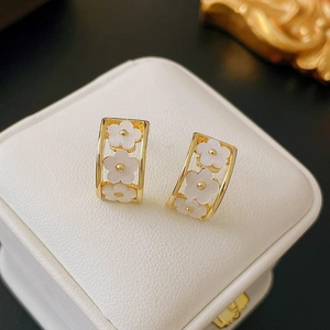 Detail of gold C-shaped earrings with white floral petals in a rectangular frame