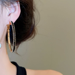Close-up of large gold circle earrings with black crystals on a model's ear