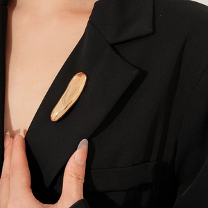 Detail view of a gold fluid metal brooch styled on a professional black blazer lapel