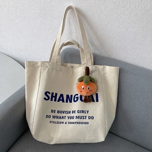 Detail of off-white canvas tote bag with blue lettering and cute orange plush charm