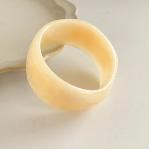 Detail view of wide beige resin bangle with clouded texture on decorative tray
