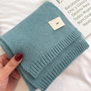 Close-up of soft turquoise knitted scarf texture featuring a small emo logo fabric label