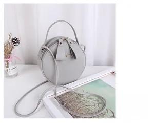 Detailed view of grey round crossbody bag featuring litchi grain texture and gold hardware