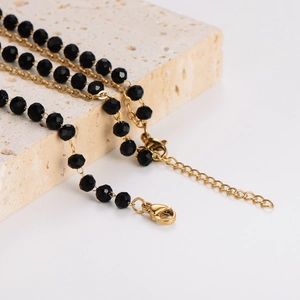 Golden chain necklace with black faceted beads draped on a beige stone, minimalist style