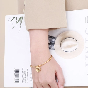 Close-up of a stylish gold heart charm bracelet worn on wrist over a beige coat